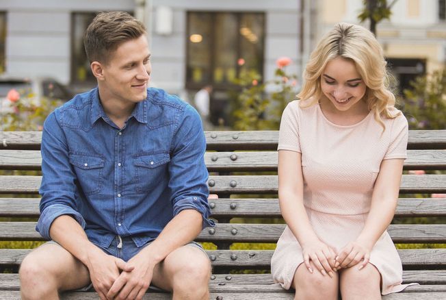 Rencontre timide - homme et femme assis sur un banc discutant et souriant.